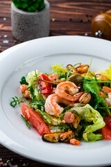 Fresh seafood salad of shrimp, mussels, cherry tomatoes oranges, grapefruits, capers, lettuce and arugula in a plate.