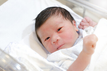 Asian cute little newborn baby opening eyes and laying in crib in prenatal hospital