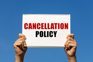 Cancellation policy text on notebook paper held by 2 hands with isolated blue sky background. This...