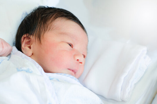 Asian cute little newborn baby opening eyes and laying in crib in prenatal hospital