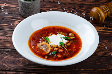 Solyanka soup with ham, meat, olives, tomatoes, sour cream, lemon, pickled cucumbers, onions and herbs.