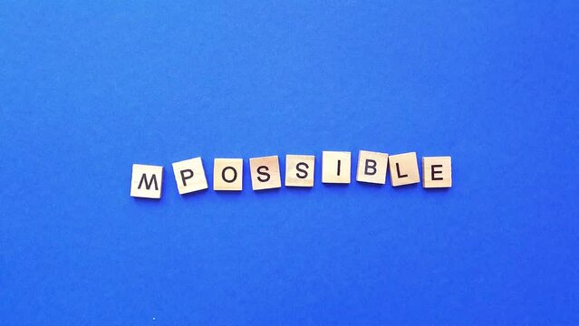 Changing the word impossible from wooden letters to possible on a blue background. top view