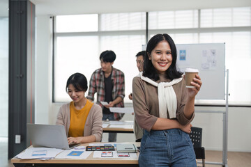 Portrait of relaxed young woman creative designer standing in office with colleagues meeting in background