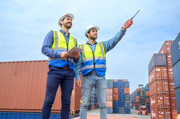 Container operator wearing white helmet and reflection shirt and holding tablet doing routine inspection while working in container yards. Logistics and shipping concept.