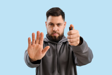 Young man with pepper spray for self-defence on blue background, closeup