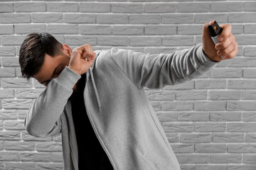Young man with pepper spray for self-defence on grey brick background