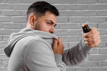 Young man with pepper spray for self-defence on grey brick background, closeup