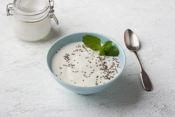 Blue ceramic bowl of yogurt sprinkled with chia seeds and garnished with mint on a light gray...