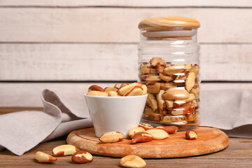 Glass jar and bowl of tasty Brazil nuts on wooden table