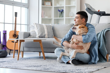 Obraz na płótnie Canvas Young man with cute Labrador dog sitting on floor at home