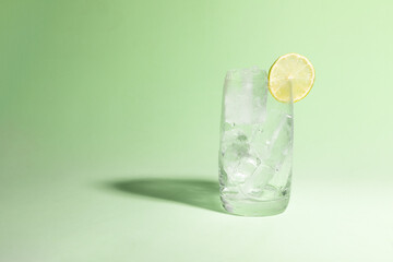 Cold glass full of ice with a lime, ready to serve light green with cast shadow.