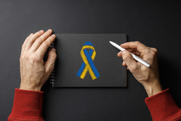 pen in my hands and yellow blue ribbon on notebook