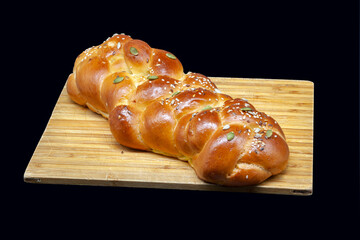 A white challah loaf on a wooden board with linseeds, sunflower seeds and pumpkin seeds. Golden freshly baked crust with highlights. Photo in high quality.
