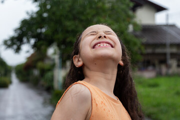 Young girl with smile is enjoying herself in the rain. Close-up of girl under the summer rain. 