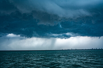 View of tropical ocean storm with menacing clouds and rain showering below, Light in the dark and dramatic storm clouds background