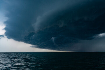 View of tropical ocean storm with menacing clouds and rain showering below, Light in the dark and dramatic storm clouds background