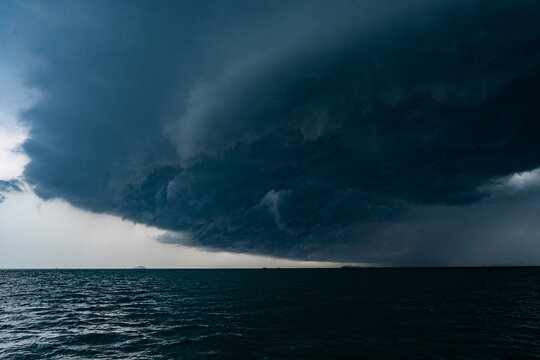 View of tropical ocean storm with menacing clouds and rain showering below, Light in the dark and dramatic storm clouds background