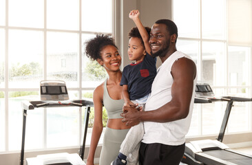 Young african american family in sportswear holding cute baby while exercising in the gym - Powered by Adobe