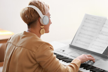 Mature female musician with headphones playing synthesizer at home