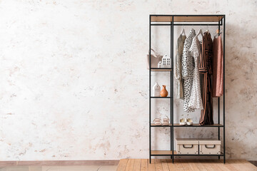 Shelving unit with clothes, shoes and bag near light wall