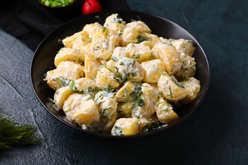 Bowl of tasty Potato Salad with greens on dark background