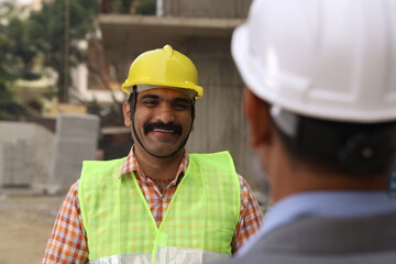 Hardworking Indian Site engineer and manager analyzing the blueprint and figuring out the work in progress. Reporting the inspector.