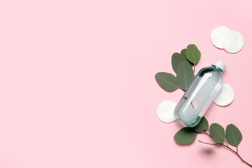 Bottle of micellar water with cotton pads and eucalyptus branch on pink background