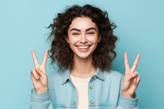 Friendly pretty woman smiling to camera and making the victory sign with his hands, isolated on pastel blue. Generative AI