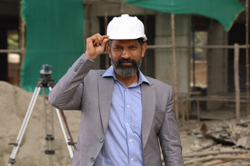 Hardworking Indian Site engineer figuring out the work in progress. On the site location wearing the uniform and helmet in white. Stylish and flamboyant engineer on the construction site, working hard