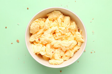 Bowl of delicious scrambled eggs on green background