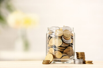 Jar with coins on wooden table against blurred background. Savings concept