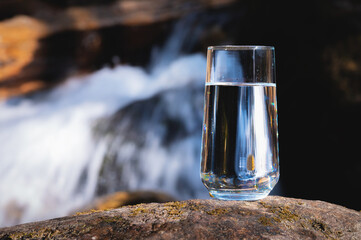 Natural water in a glass. Pure water in a transparent glass against the backdrop of a mountain river in the background. Healthy food and clean natural water