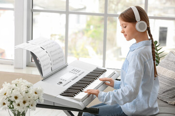Little girl in headphones playing synthesizer at home