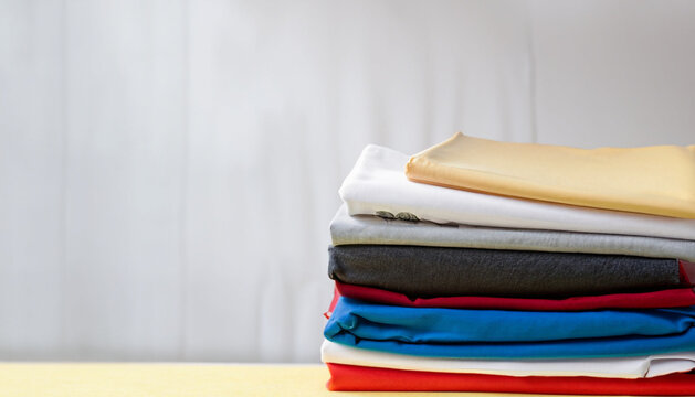 stack of colorful clothes, White table , blue, red, yellow, white, gray, brown, black, unstitched fabrics clothes top on table, Blurred white background, Ai Generate 