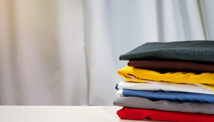 stack of clothes on a hanger, stack of colorful clothes, White table , blue, red, yellow, white, gray, brown, black, unstitched fabrics clothes top on table, Blurred white background, Ai Generate 