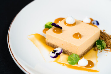 Delicious, colorful dessert decorated with edible flower petals on a white plate against a dark background.