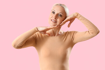 Mature woman doing face building exercise on pink background