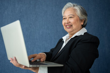 Portrait of intelligent senior businesswoman CEO manager holding laptop creating a presentation on isolated blue background. Old Woman is happy and smile after getting financial statements reports