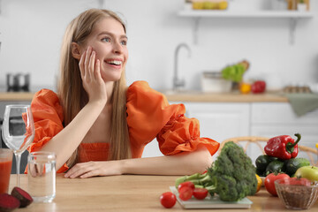 Young woman with fresh vegetables and blender in kitchen