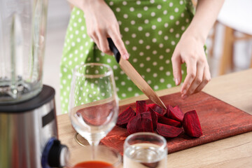 Young woman cutting beet in kitchen, closeup