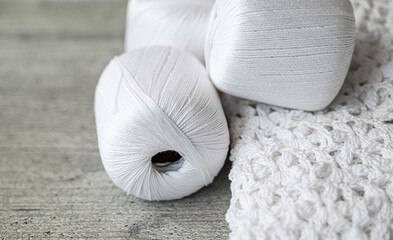 white lace knitting and 3 skeins of cotton threads on a gray wooden surface