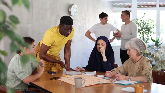 Happy african american man playing board game with group of friends at table. Adult socialization concept