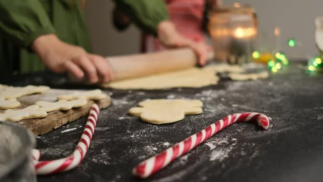Girl rolling dough for homemade gingerbread with christmas candy cane on foreground