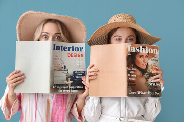 Young sisters in summer hats reading magazines on blue background