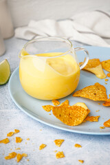 Plate with pitcher of tasty cheddar cheese sauce and nachos on white grunge background