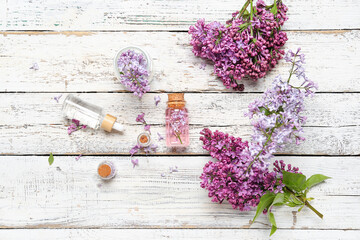 Composition with bottles of lilac essential oil and flowers on light wooden background