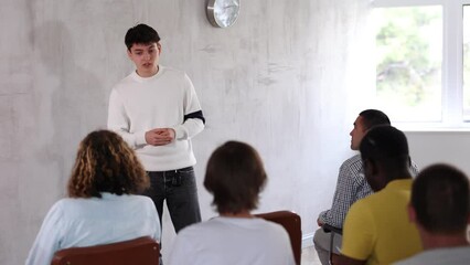Motivated young student presenting report to group of fellow male students sitting in auditorium of educational institution