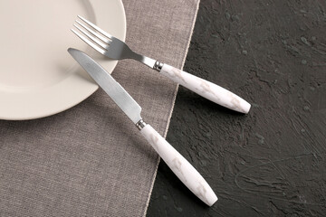 Plate with stainless steel fork and knife on black background