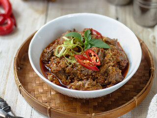 Tumis Daging Sapi Mercon or Stir fry or saute of beef with onion, red cayenne pepper and other herb and seasoning. Serving in white plate on wooden table. Indonesian food, recipe and cuisine