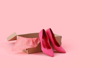 Cardboard box with stylish high-heeled shoes on pink background